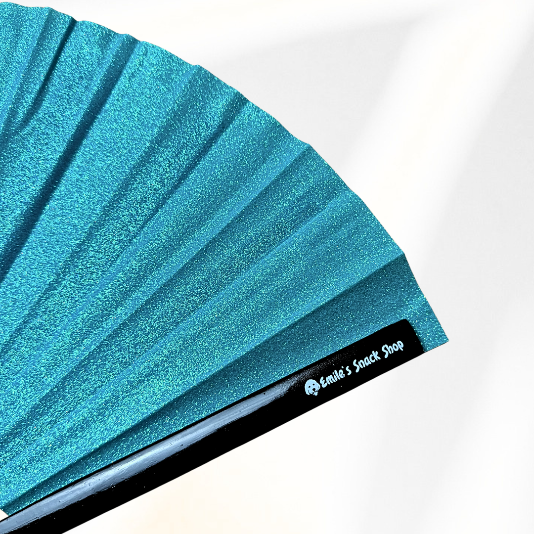 A close-up of a turquoise blue glitter folding fan with black ribs, showing the brand name &